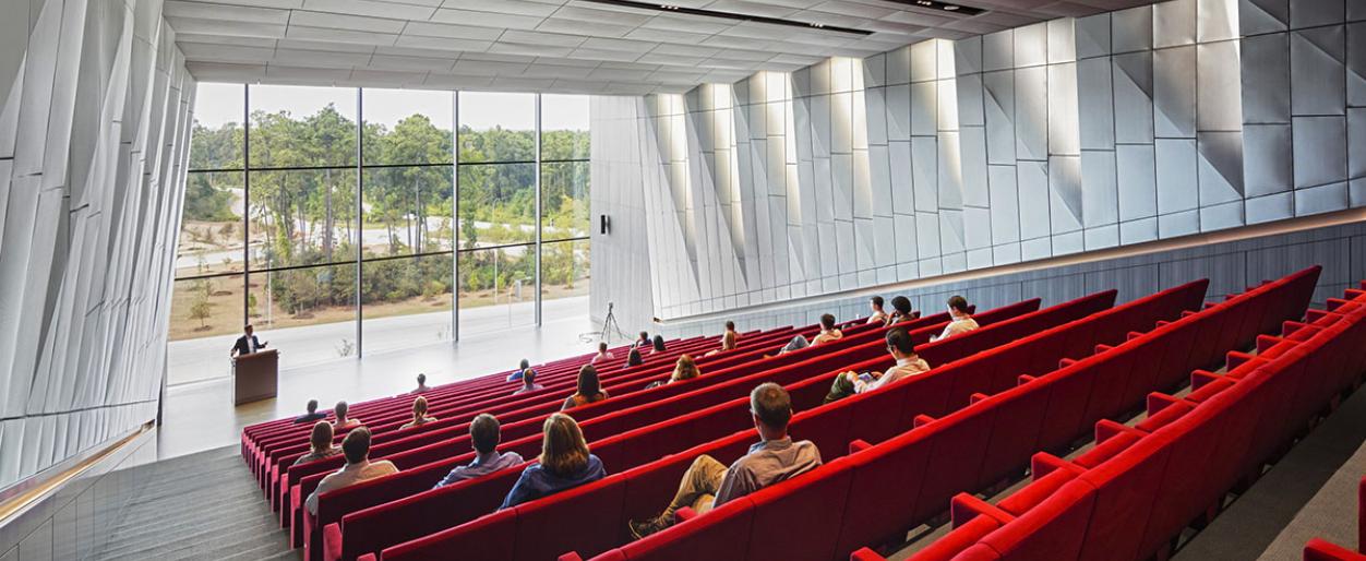 Interior view of a modern corporate auditorium with red seating and large floor-to-ceiling windows, designed by Pickard Chilton for corporate headquarters