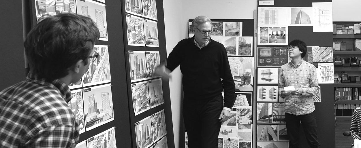 William D Chilton discussing the prospects of various designs pinned on a board with his colleagues.