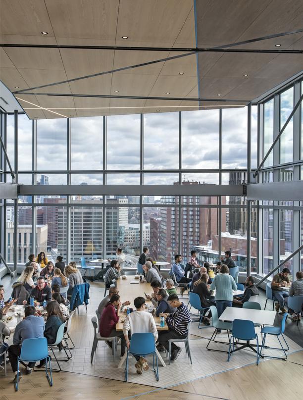 lots of open glass with people sitting on cafeteria style tables looking out at Cambridge Ma from the Akamai Headquarters building