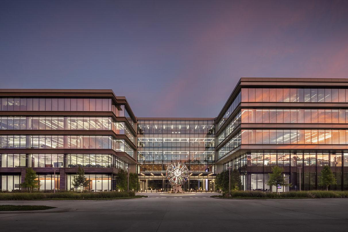 Exterior of Hewlett Packard Enterprise's Houston campus at dusk, showcasing a modern glass façade, connected buildings, and a central illuminated sculpture.