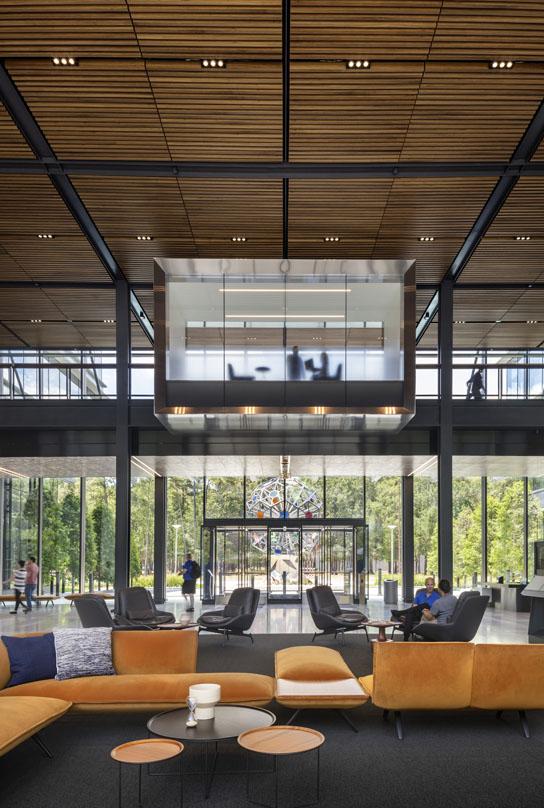Interior of Hewlett Packard Enterprise's Houston campus, featuring an open, modern lobby with floor-to-ceiling glass, contemporary seating, and a suspended meeting room.