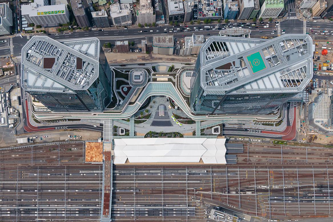 Aerial view of the Takanawa Gateway City construction site, showing two skyscrapers, cranes, and various construction materials and structures.