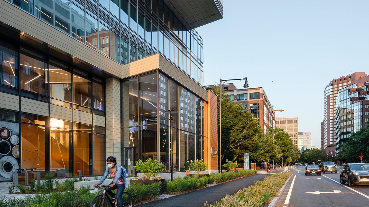 a person riding a bike on the sidewalk in front of the Akamai building in Cambridge Mass