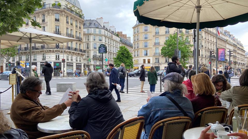 People enjoy dining outdoors at a Parisian cafe with bustling street views of classic Paris architecture and passersby in the background